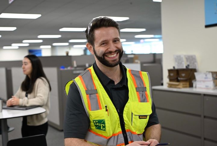 An S&C team member wearing a safety vest smiles for the camera An S&C team member wearing a safety vest smiles for the camera