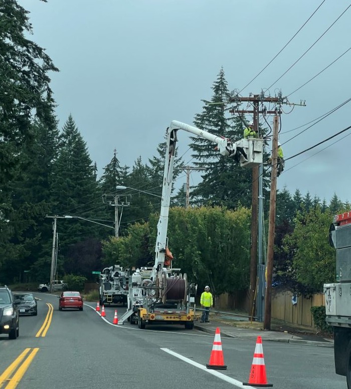 Utility crews working from bucket trucks to repair overhead power lines along a roadside following a service disruption.